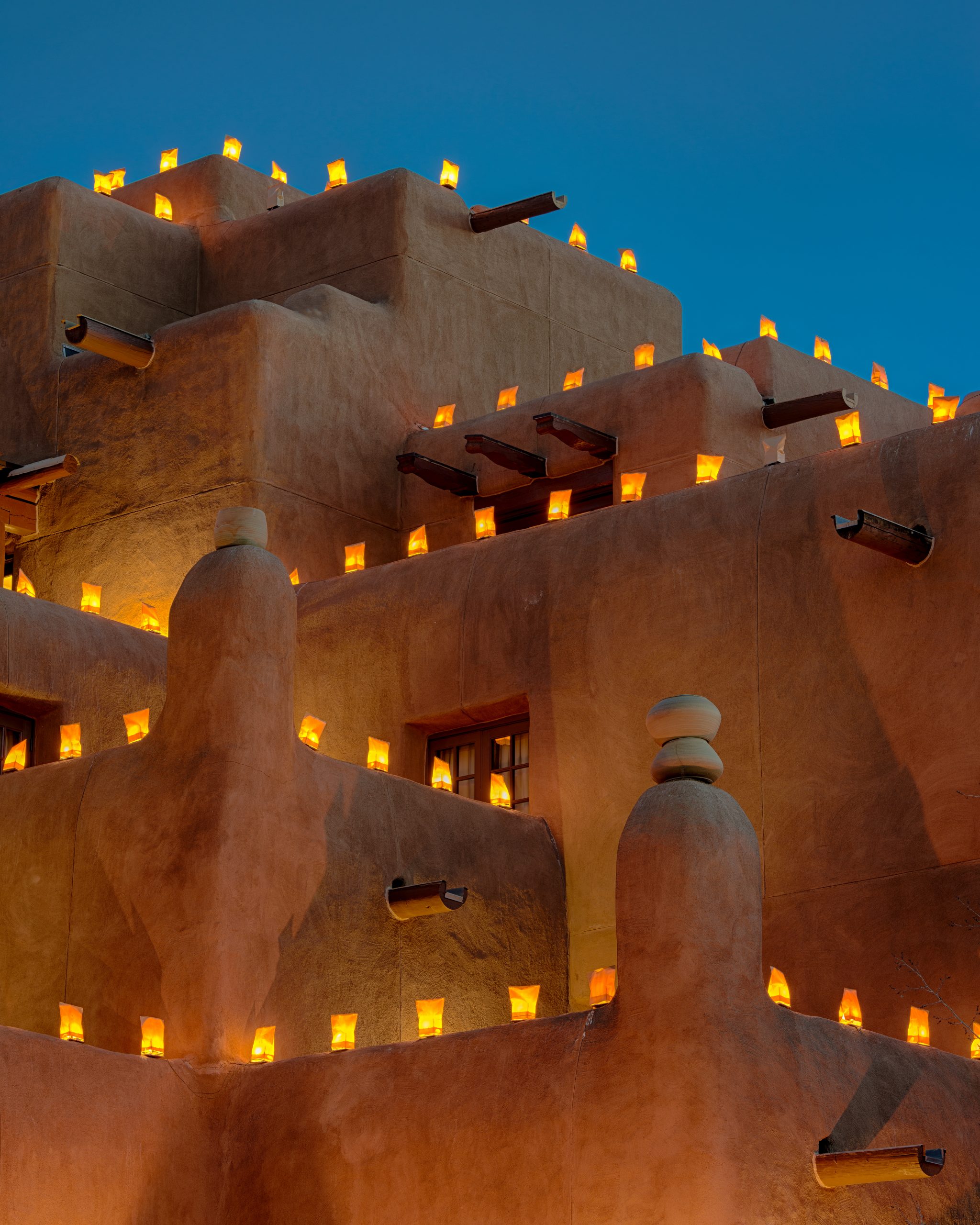 Luminaria on adobe building Trail with hot air balloon and mountains in background